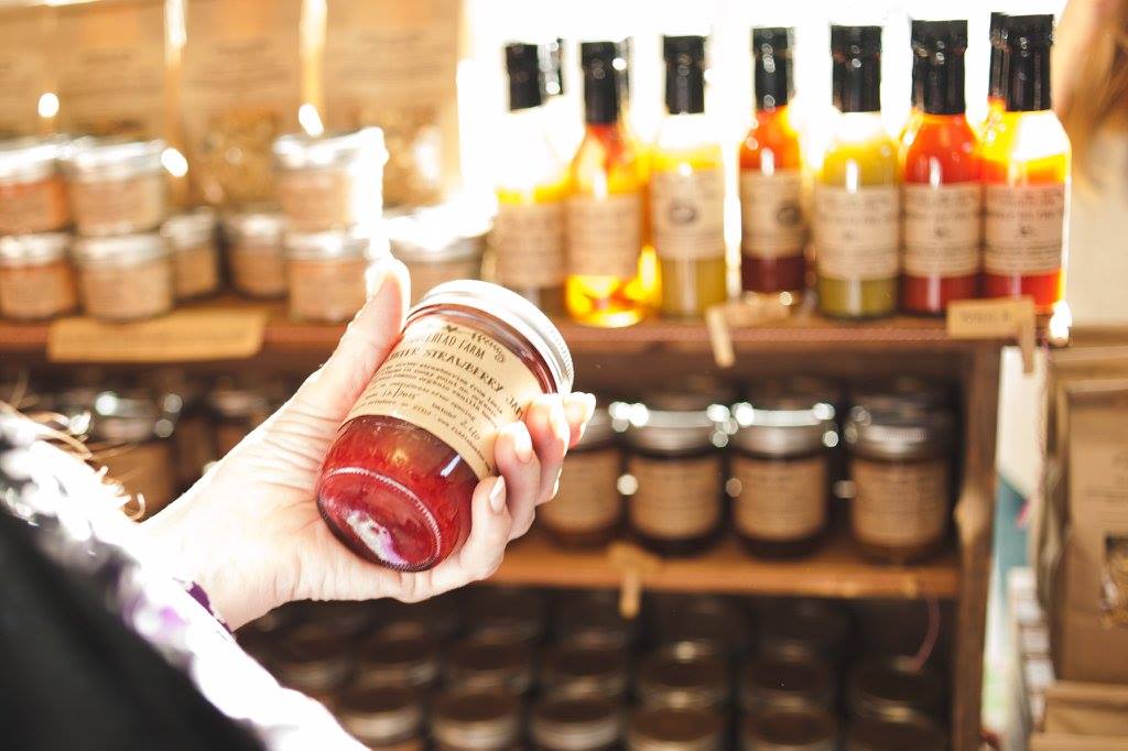 A woman holding a jar of Fiddlehead Farm jam in front of a display of jam.